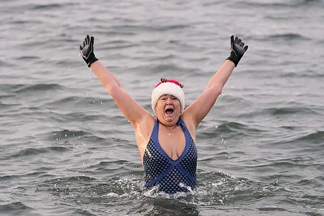 A woman in the sea raises her arms above her head 