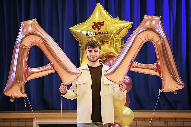 Year 14 student Shane Bunting, who was awarded two As and a C in his A-levels, holds two inflatable As in celebration at his college, Hazelwood Integrated in Newtownabbey, Belfast