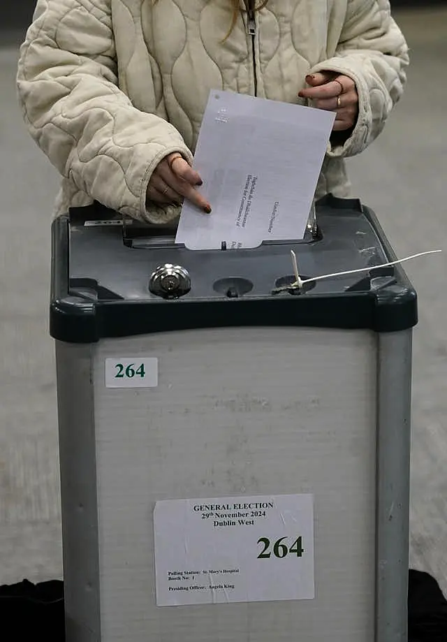 A woman in a white coat drops her vote into a ballot box