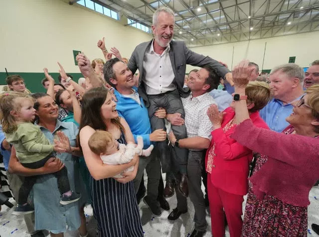 A group of people hoist a gentleman in a suit into the air on their shoulders. 