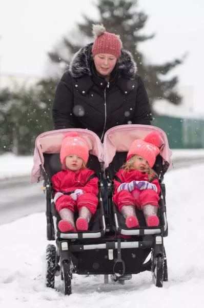A mother pushes her twins through the snow in their buggy