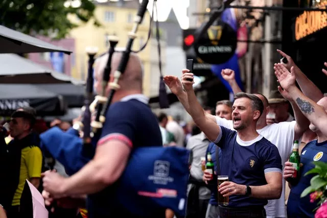 A Scotland fan plays the bagpipes while others sing with their hands in the air