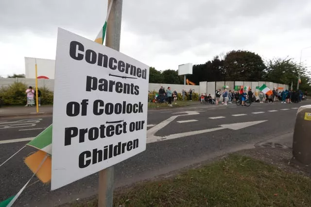 A sign at the Crown Paints factory reading 'Concerned parents of Coolock protect our children' as protesters can be seen in the background