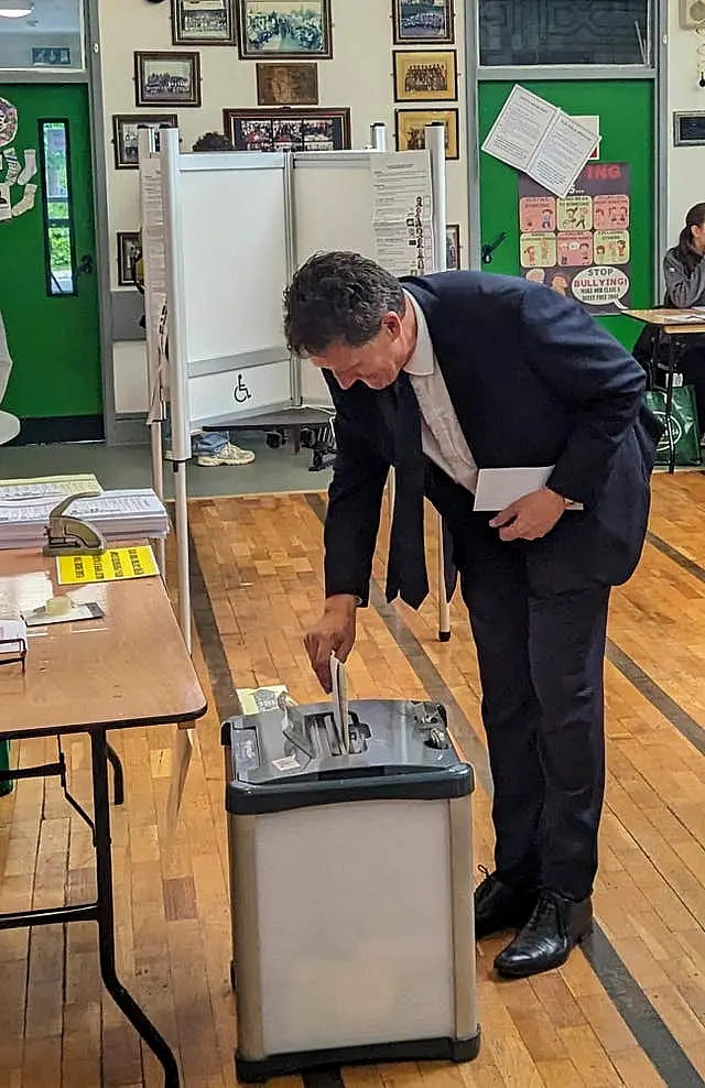 Green party leader Eamon Ryan bends over to put his voting slip inside the box. He's wearing a suit and is in a school hall or gym