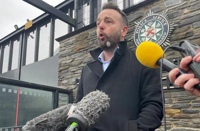 Colum Eastwood speaking into microphones being held out by members of the media outside a PSNI station