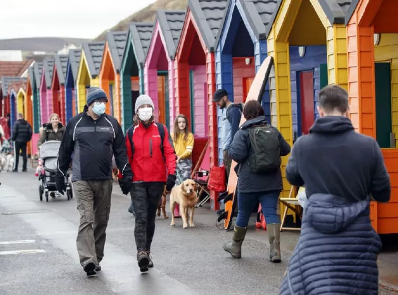 People wear face masks as they walk past beach huts in Saltburn-by-the-Sea