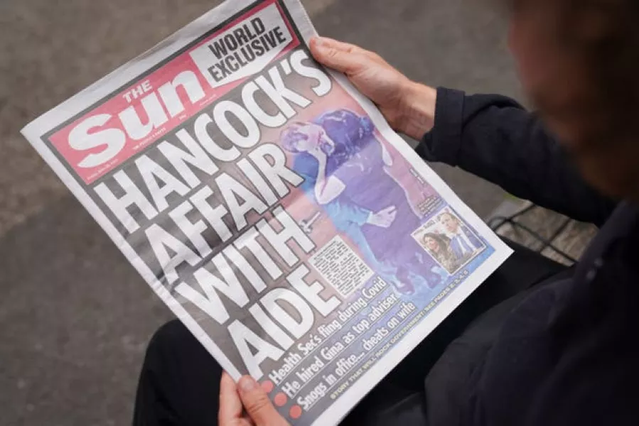 A person reads a copy of Friday's Sun newspaper, with the story and pictures of Health Secretary Matt Hancock appearing to kiss his adviser Gina Coladangelo 