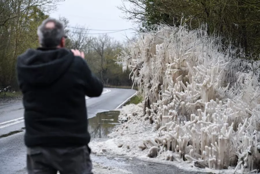 A passerby stops to take a photograph of ice formations on a roadside near Sandridge, Hertfordshire
