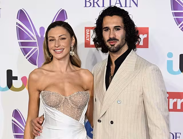 A woman in a strapless dress and a man in a beige jacket stand together