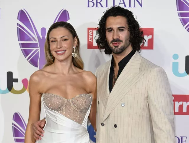 A woman in a strapless dress and a man in a beige jacket stand together