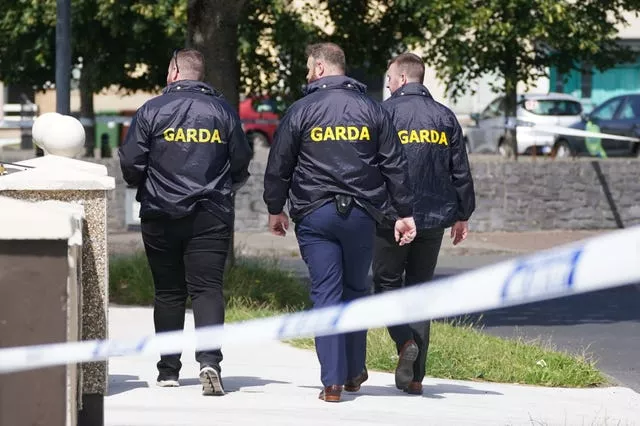 Three officers in black coats with the word Garda on the back seen from behind