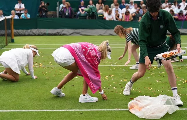 Katie Boulter helps ground staff clear confetti from court 18 