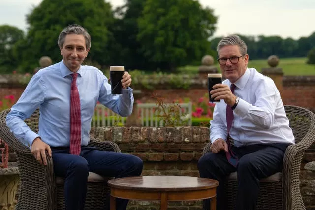 Taoiseach Simon Harris and Sir Keir Starmer each raise a glass of Guinness while sitting down at a table in the garden at Chequers