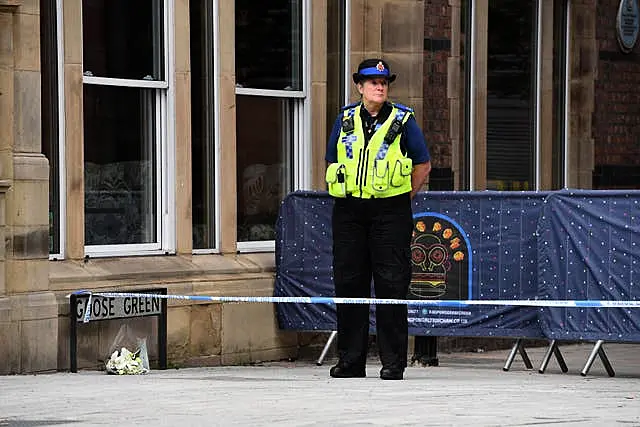 A PCSO stands alongside a floral tribute at the scene in Railway Street in the Goose Green area of Altrincham, Trafford, where 31-year-old Rico Burton, the cousin of heavyweight boxing champion Tyson Fury, died following an alleged stabbing incident