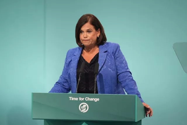 Mary Lou McDonald in a blue blazer stands at a blue lectern making a speech. 