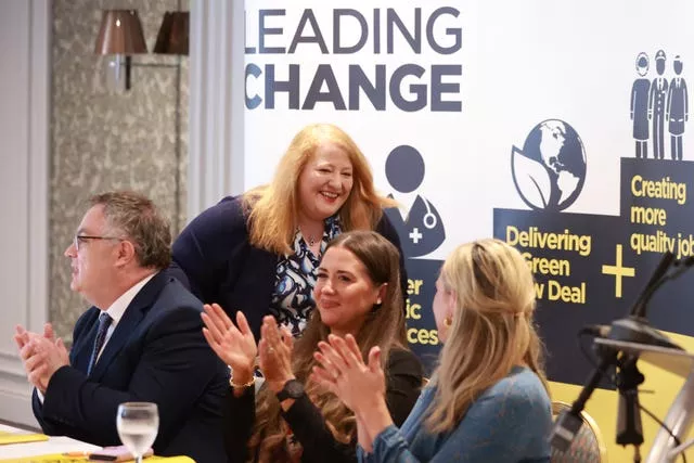 Naomi Long walks behind parliamentary candidates who are seated