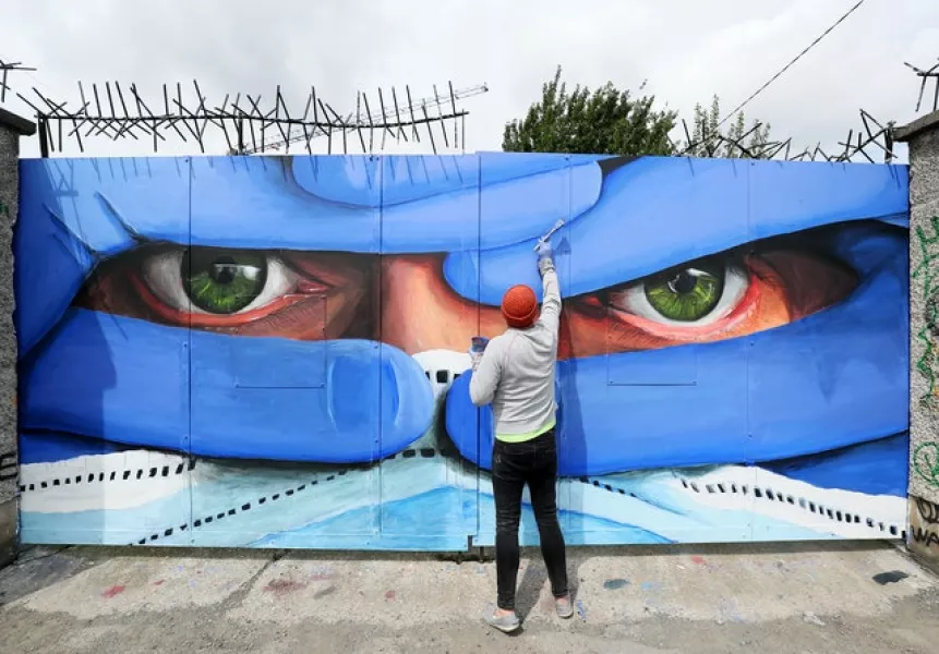 Dublin-based artist Asbestos puts the finishing touches to the latest in his series of mask portraits. Photo: Brian Lawless/PA