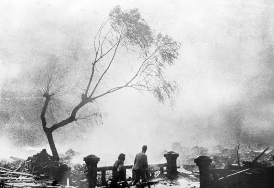 Survivors walk through the destruction as fire rages in the background (AP)