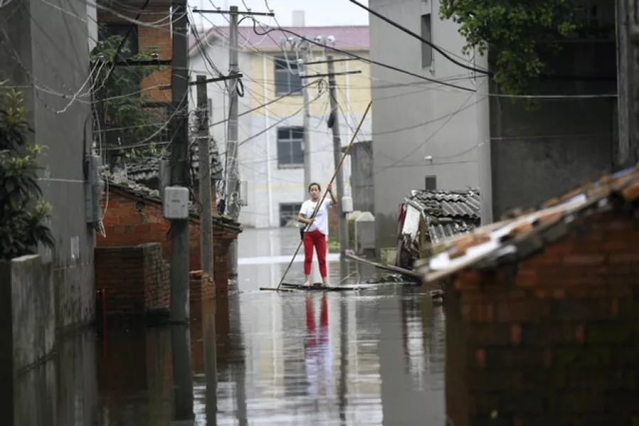 A woman pushes a makeshift raft down a flooded alleyway in a village in Yongxiu (Chinatopix via AP)