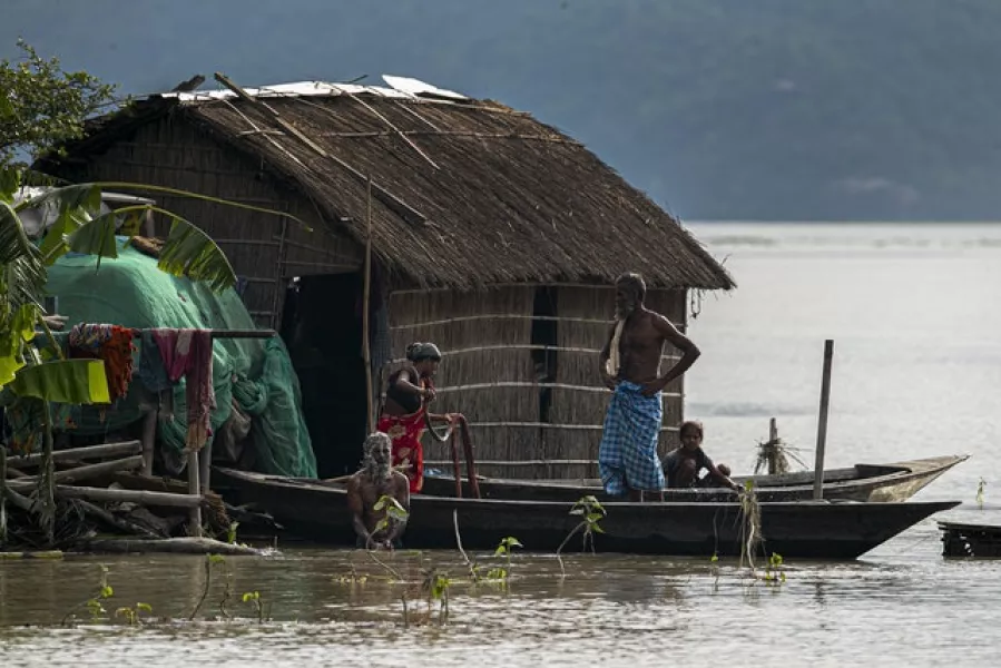 A family takes shelter on a boat near their partially submerged house in Assam, India (Anupam Nath/AP)