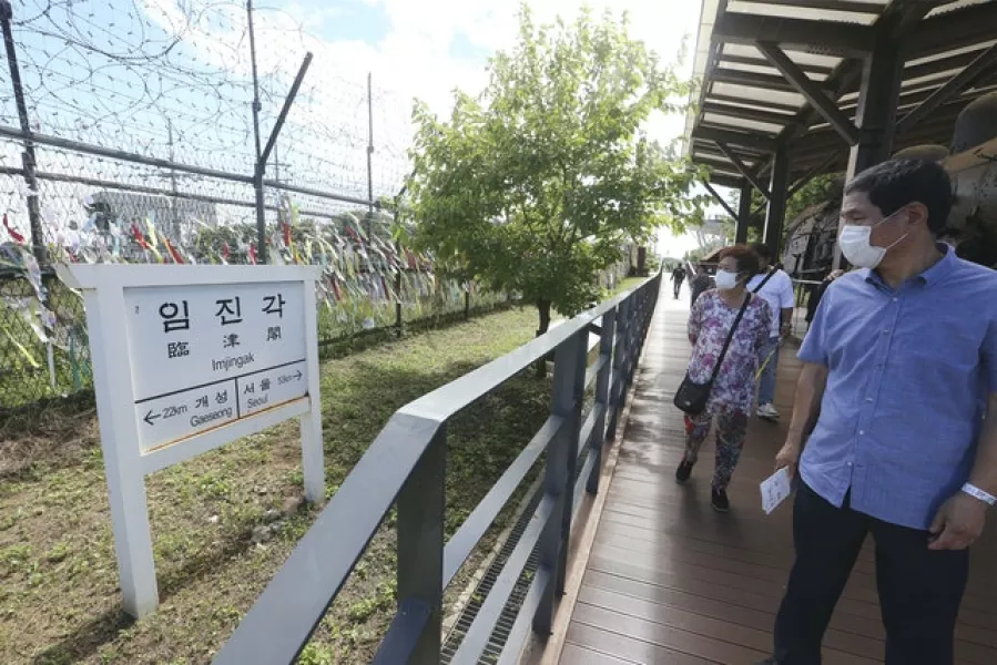 People wearing face masks pass a sign showing the distance to North Korea’s city Kaesong and South Korea’s capital Seoul at the Imjingak Pavilion in Paju, near the border with North Korea (Ahn Young-joon/AP)