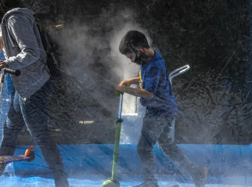 A child wearing a protective face mask makes his way on his scooter through a decontamination chamber as a precaution against the spread of the new coronavirus (AP)