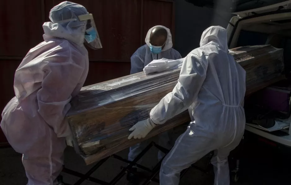 Funeral home workers in protective suits carry the coffin of a woman who died from Covid-19 into a hearse in Katlehong, near Johannesburg, South Africa (Themba Hadebe/AP)