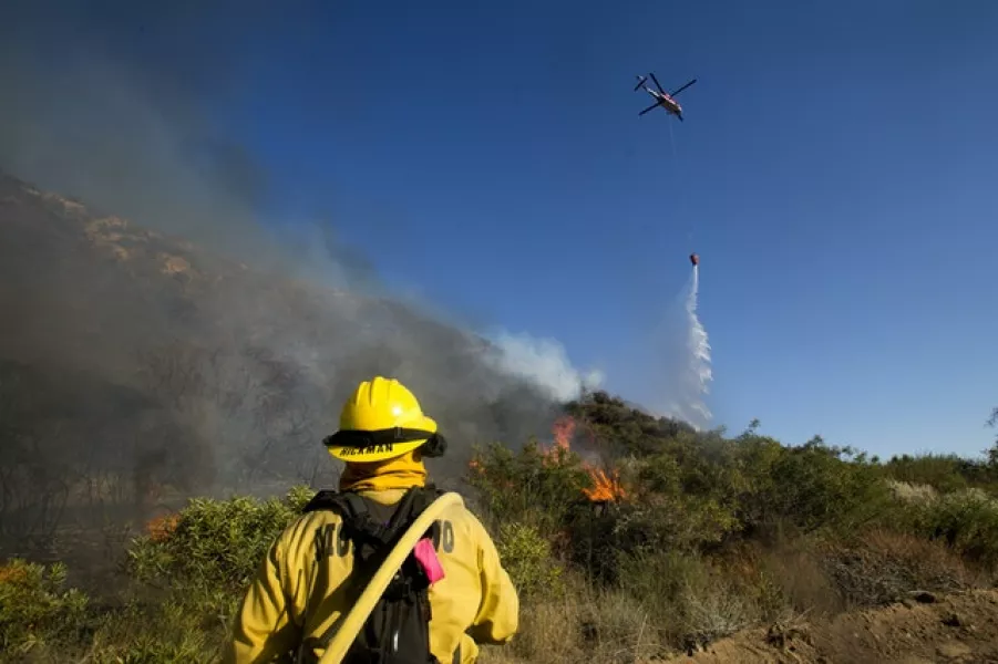A firefighter watches as a helicopter drops water on to the fire (Ringo H W Chiu/AP)