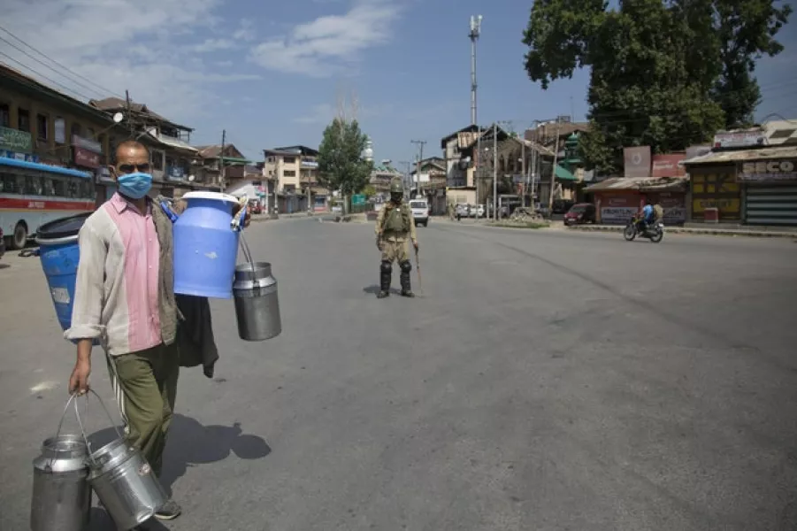 A Kashmiri milkman walks past a paramilitary soldier during curfew (Mukhtar Khan/AP)