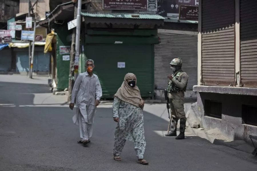 Kashmiris walk past a paramilitary soldier (Mukhtar Khan/AP)