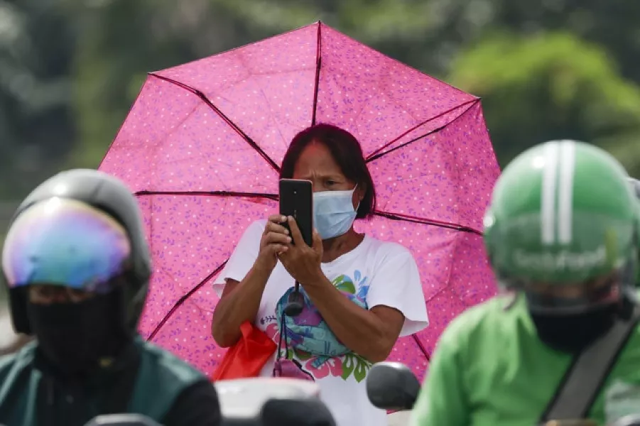 A woman wearing a mask takes a photo of a checkpoint (Aaron Favila/AP)
