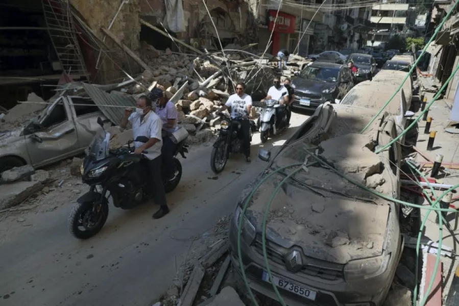 People drive past buildings and cars that were damaged (Bilal Hussein/AP)
