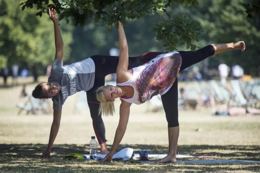 Two women perform yoga exercises in a shaded spot in Green Park, central London (Victoria Jones/PA)
