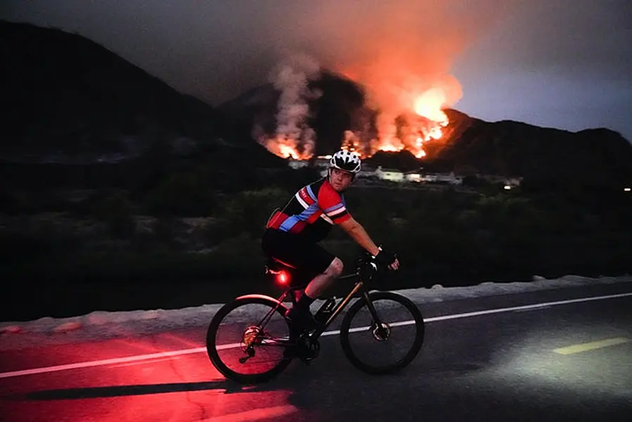 A cyclist rides along a trail as the fire burns in California (Marcio Jose Sanchez/AP)