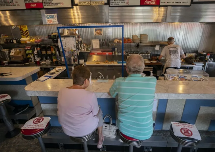 Regulars Barbara and Doug Lovett wait for their cheese burgers surrounded by Covid-19 protective measures as August Muzzi, owner of Angelo’s Luncheonette, works at the grill in Wilmington, Delaware (Carolyn Kaster/AP)