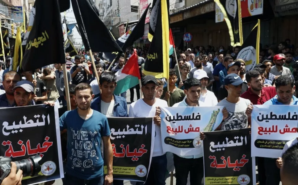 Protesters hold placards as others wave their black flags during a demonstration in Gaza City against the Israel-United Arab Emirates deal (Adel Hana/AP)
