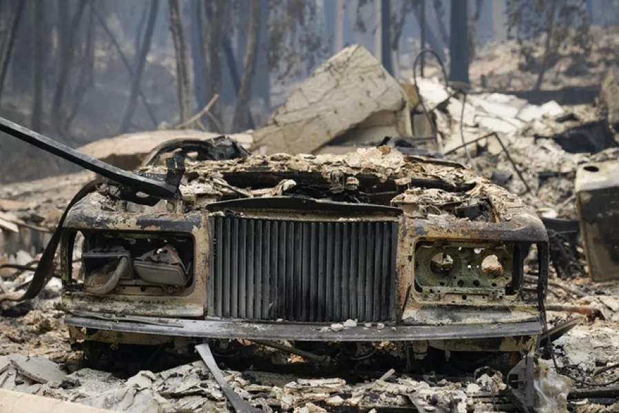 A charred vehicle is parked in front of a home in Boulder Creek, California (Marcio Jose Sanchez/AP)