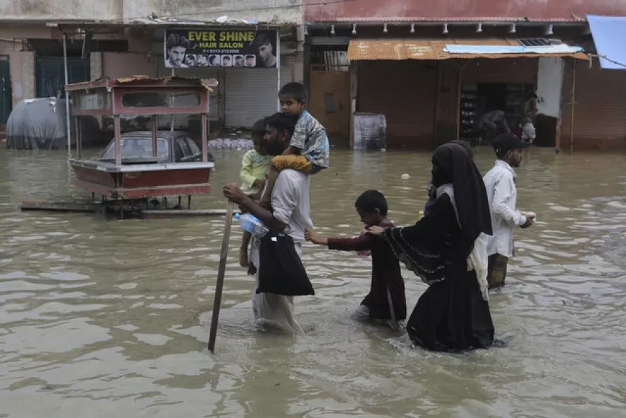 Local residents wade through a flooded area caused by heavy rainfall in Karachi (AP/Fareed Khan)