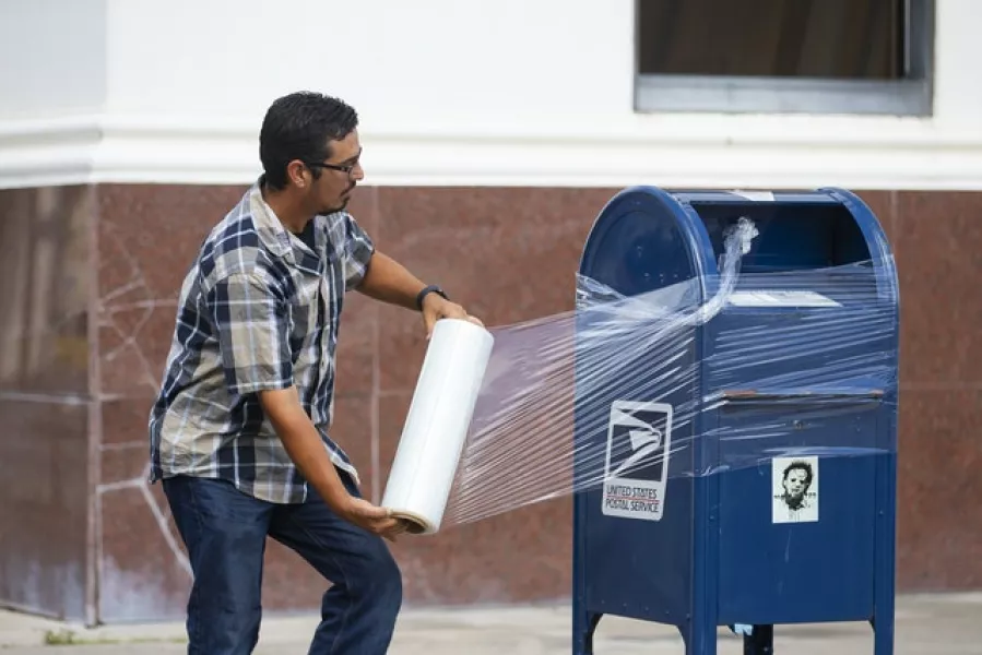 A United State Postal Service employee covers a post box with plastic wrap after removing its contents in anticipation of Hurricane Laura (Mark Mulligan/Houston Chronicle via AP)