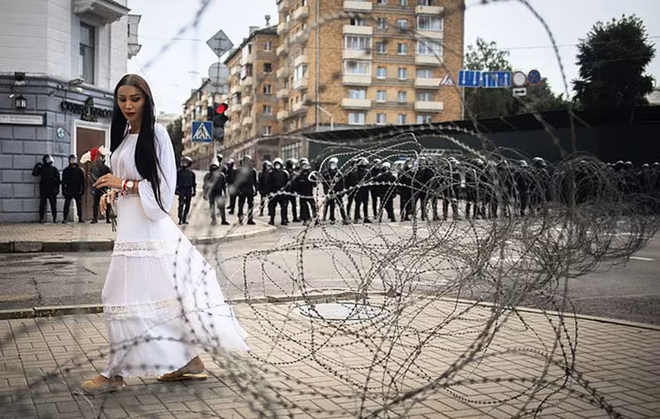 A woman walks past the barbed wire separating Belarusian servicemen and Belarusian opposition supporters during a rally in Minsk (AP)