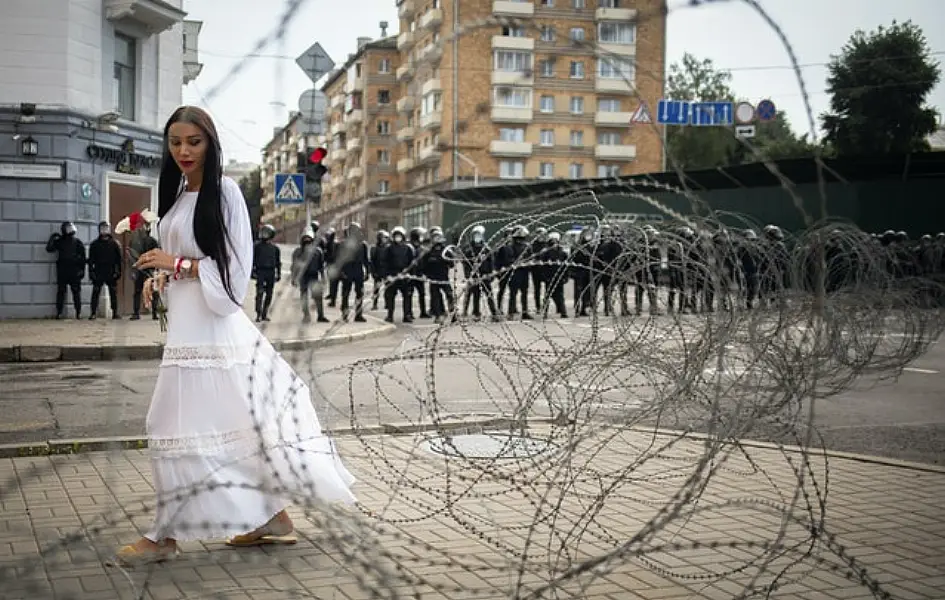 A woman walks past the barbed wire separating Belarusian servicemen and Belarusian opposition supporters during a rally in Minsk (AP)