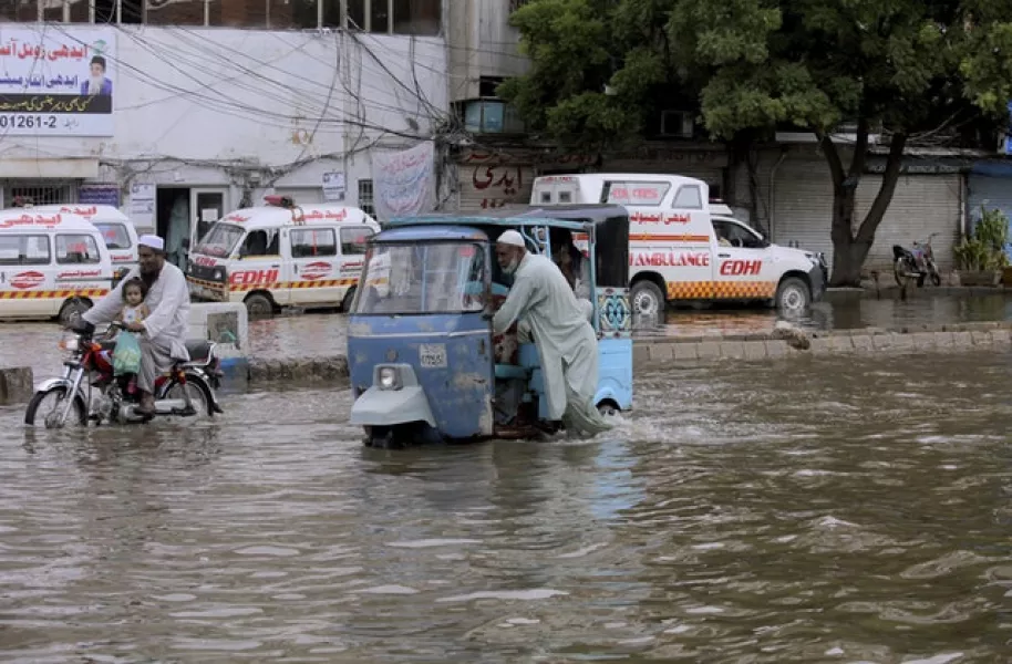 A driver pushes his motorised rickshaw through floodwater in Karachi (Fareed Khan/AP)