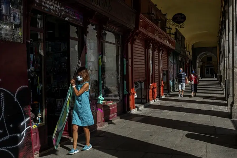 A woman, wearing protective masks to prevent the spread of the coronavirus, opens a commercial store in the Plaza Mayor, in the centre of Madrid (Bernat Armangue/AP)