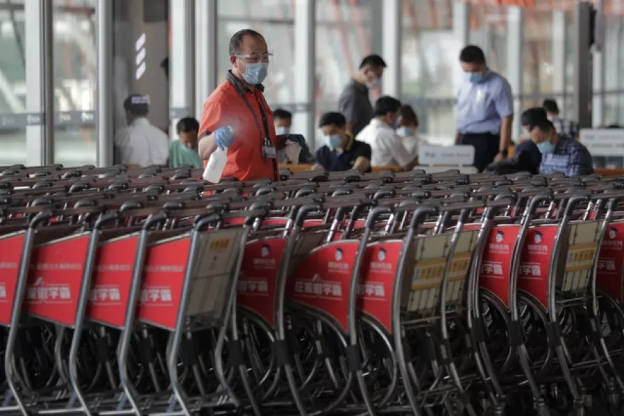 A worker wearing a face mask to help curb the spread of the coronavirus sprays disinfectant on the trolleys at the departure hall of Beijing Capital International Airport (Andy Wong/AP)