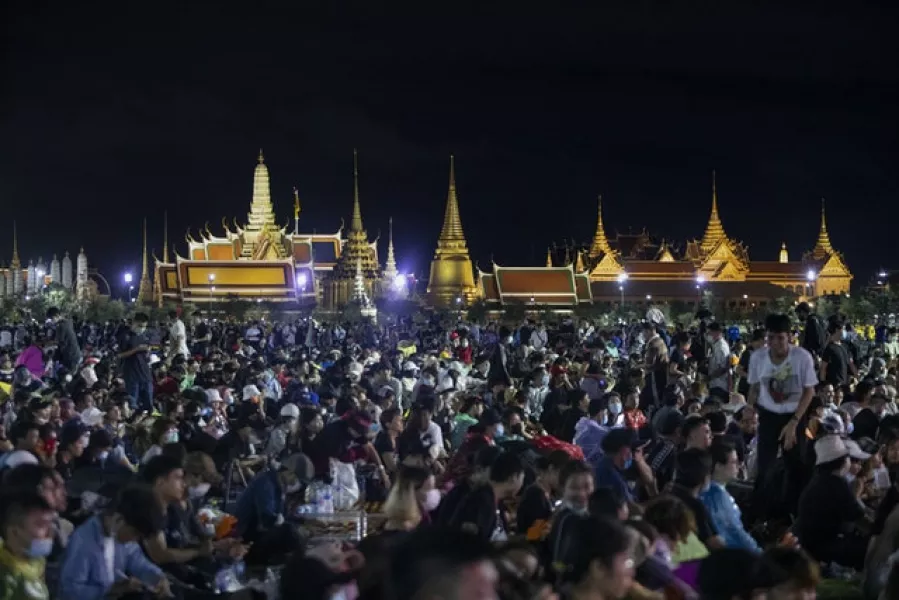 Pro-democracy demonstrators attend a protest with The Grand Palace lit up in the background (Sakchai Lalit/AP)