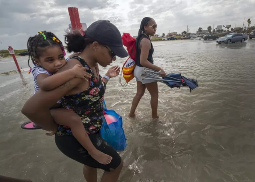A woman gives her daughter a piggyback ride across a flooded area in Galveston, Texas (Stuart Villanueva/The Galveston County Daily News via AP)