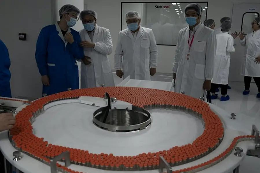 Visitors and workers chat as they look at vials of the Covid-19 vaccine at the SinoVac  factory (Ng Han Guan/AP)