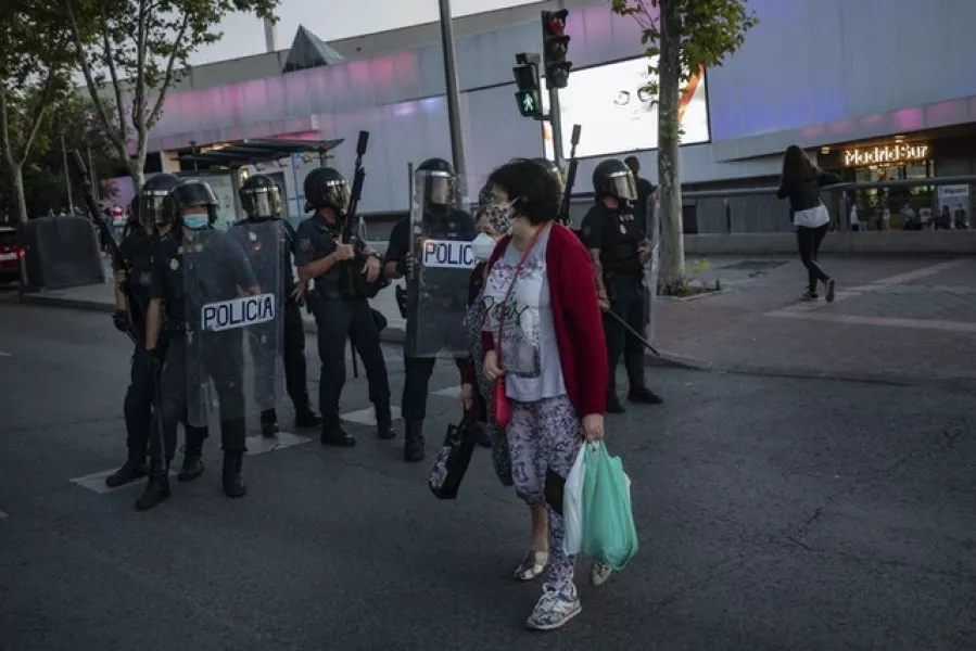 A woman cross the street in front a riot police unit in Madrid (Bernat Armangue/AP)