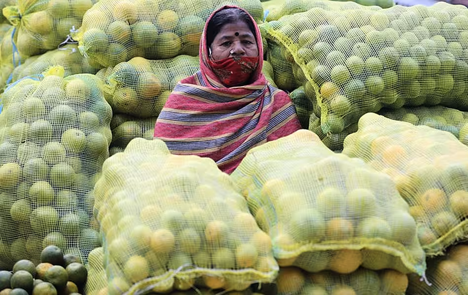 A fruit vendor wearing a face mask sits amid sacks of oranges at a wholesale market in Bengaluru (Aijaz Rahi/AP)