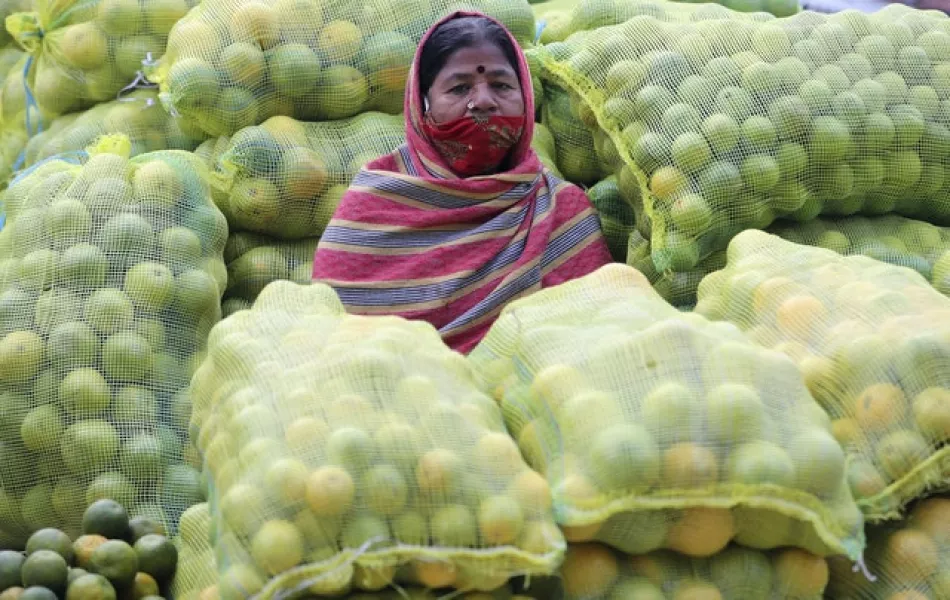 A fruit vendor wearing a face mask sits amid sacks of oranges at a wholesale market in Bengaluru (Aijaz Rahi/AP)